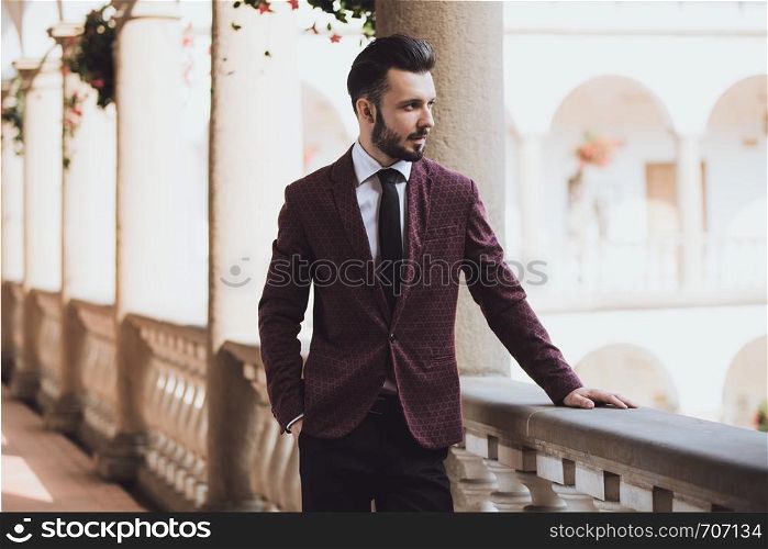 Elegant and fashionable businessman in jacket standing on the balcony of classical architecture building.
