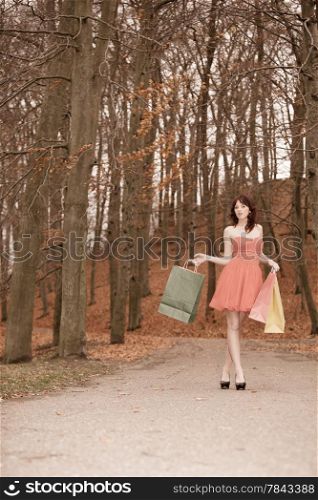 Elegant autumn shopper woman with sale bags outdoor in park after shopping. Vintage photo, sepia tone