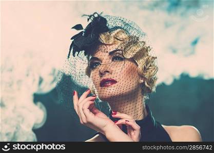 Elegant blond retro woman wearing little hat with veil in smoke