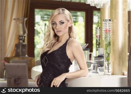 elegant blond woman in black dress waiting for people near a cafe in a luxury restaurant, she is posing