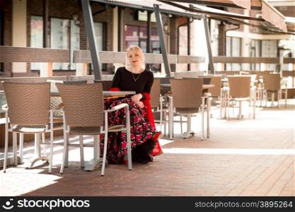 Elegant blonde woman in long dress sitting on summer terrace at cafe