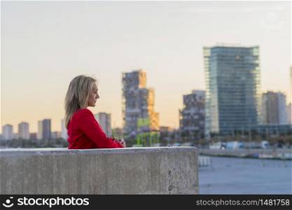 Elegant blonde woman leaning on a wall while relaxing with cityscape background