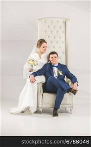 Elegant bride and groom posing on white chair at studio