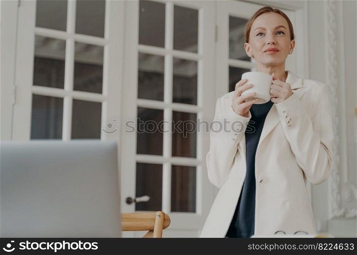Elegant business lady in formal wear is working at home or office in evening. Glamorous mid adult businesswoman is dreaming with cup of tea. Attractive european woman is a boss or entrepreneur.. Glamorous mid adult businesswoman is dreaming with cup of tea. Attractive european woman is a boss.