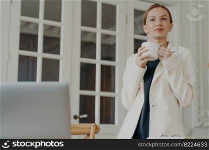 Elegant business lady in formal wear is working at home or office in evening. Glamorous mid adult businesswoman is dreaming with cup of tea. Attractive european woman is a boss or entrepreneur.. Glamorous mid adult businesswoman is dreaming with cup of tea. Attractive european woman is a boss.