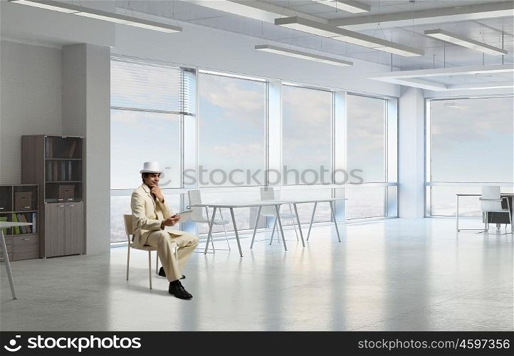 Elegant businessman using tablet. Handsome young businessman in white suit sitting in office chair and using tablet