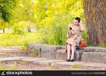 Elegant businesswoman sitting on a stone wall during a sunny spring day, and setting her hair looking herself in a little mirror