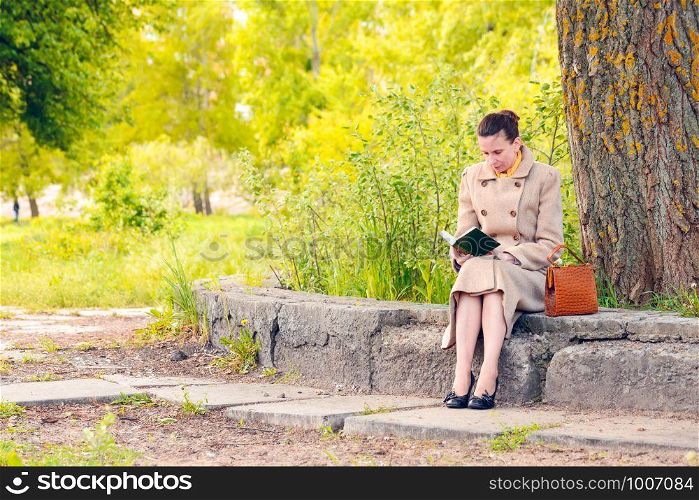 Elegant businesswoman sitting on a stone wall during a sunny spring day, and reading an adventure book