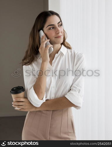 elegant businesswoman talking phone while holding coffee cup