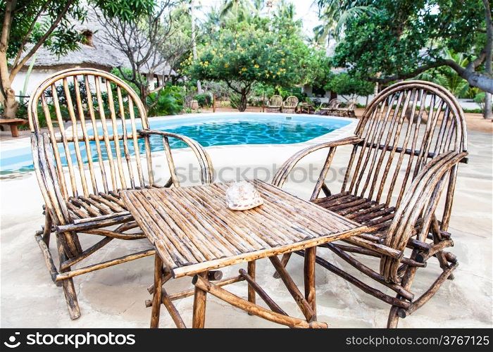 Elegant chairs made of wood close to a swimming pool inside a Kenyan garden