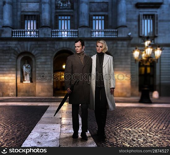 Elegant couple in coats against building facade in evening