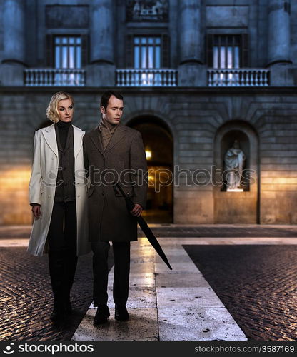 Elegant couple in coats against building facade in evening