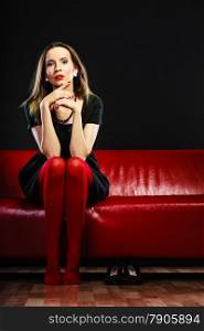 Elegant fashion outfit. Fashionable woman in vivid color pantyhose sitting on red couch indoor on black