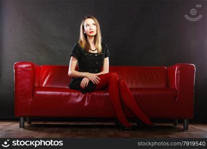 Elegant fashion outfit. Fashionable woman long legs in red vivid color pantyhose relaxing on couch indoor on black