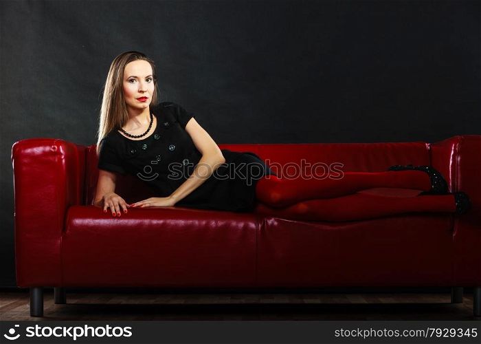 Elegant fashion outfit. Fashionable woman long legs in red vivid color pantyhose relaxing on couch indoor on black