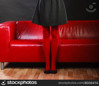 Elegant fashion outfit. Fashionable woman long legs in red vivid color pantyhose black shoes on couch indoor