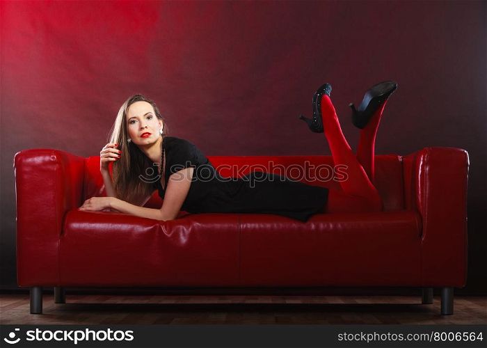 Elegant fashion outfit. Fashionable woman long legs in red vivid color pantyhose relaxing on couch indoor