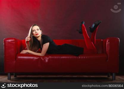 Elegant fashion outfit. Fashionable woman long legs in red vivid color pantyhose relaxing on couch indoor