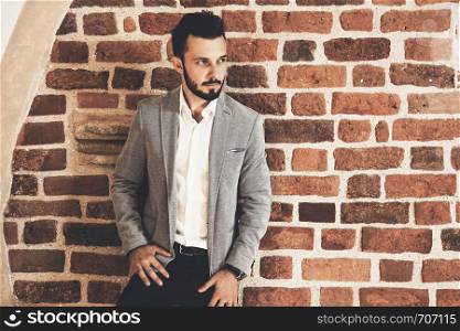 Elegant fashionable man in a jacket posing on the background of an old archival brick wall
