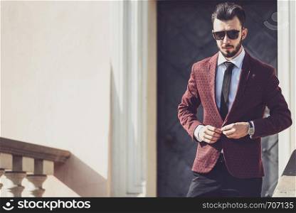 Elegant fashionable man in black sun glasses buttons his jacket outside (copy space).