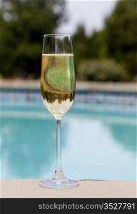 Elegant flute glass of sparkling white wine or champagne by side of swimming pool