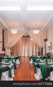 Elegant function hall prepaired for a wedding party in soft white and cream colours with a dark green as key colour.