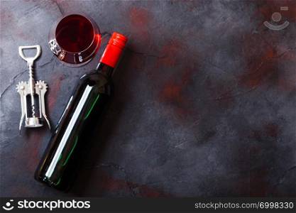 Elegant glass and bottle of red wine with corkscrew opener on kitchen table background.