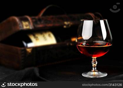 elegant glass of cognac and bottle in wooden case background