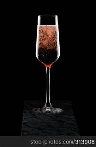 Elegant glass of pink rose champagne with bubbles on black marble board on black.