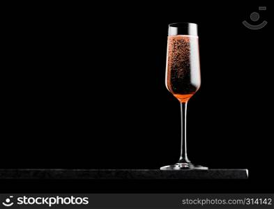 Elegant glass of pink rose champagne with bubbles on black marble board on black.