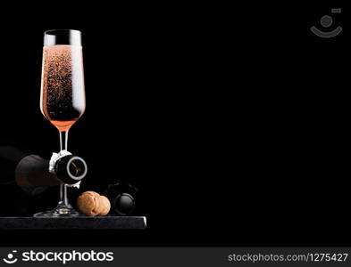 Elegant glass of pink rose champagne with cork and wire cage and bottle on black marble board on black background.