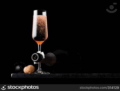 Elegant glass of pink rose champagne with cork and wire cage and bottle on black marble board on black background.