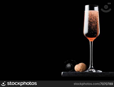 Elegant glass of pink rose champagne with cork and wire cage on black marble board on black background.