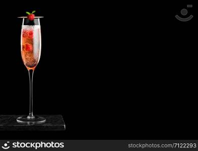 Elegant glass of pink rose champagne with raspberries inside on black marble board on black background.