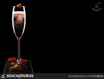 Elegant glass of pink rose champagne with raspberry on stick with fresh berries and mint leaf on black marble board on black.