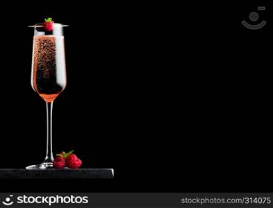 Elegant glass of pink rose champagne with raspberry on stick with fresh berries and mint leaf on black marble board on black background.