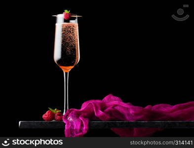 Elegant glass of pink rose champagne with raspberry on stick with fresh berries and mint leaf on black marble board on black background.