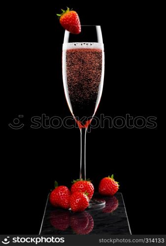 Elegant glass of pink rose champagne with strawberry on top on black marble board on black.