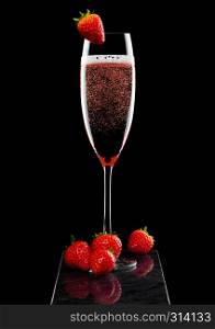 Elegant glass of pink rose champagne with strawberry on top on black marble board on black.