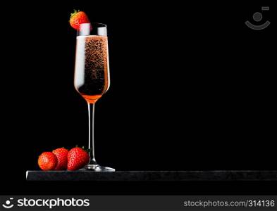 Elegant glass of pink rose champagne with strawberry on top on black marble board on black background.