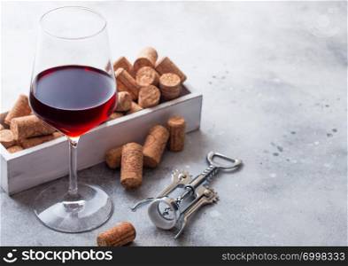 Elegant glass of red wine with box of corks and opener on kitchen table background.
