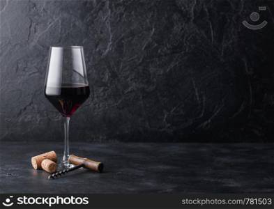 Elegant glass of red wine with corks and corkscrew on black stone background.