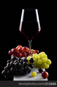Elegant glass of red wine with dark and red and green grapes on wooden board on black background.