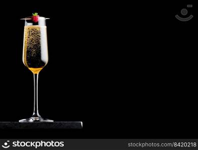Elegant glass of yellow ch&agne with rasspbery on stick on black marble board on black background. 