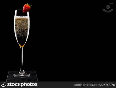 Elegant glass of yellow ch&agne with strawberry on top on black marble board on black background. 