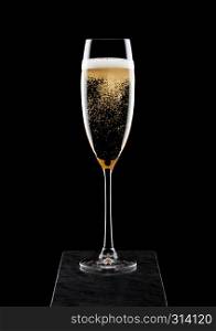 Elegant glass of yellow champagne with bubbles on black marble board on black.