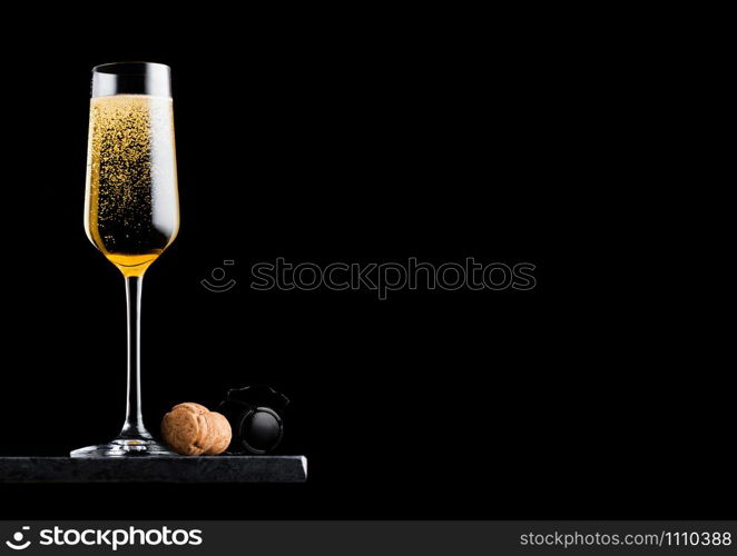 Elegant glass of yellow champagne with cork and wire cage on black marble board on black background.