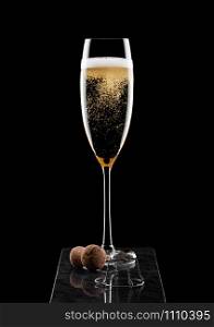 Elegant glass of yellow champagne with cork and wire cage on black marble board on black.