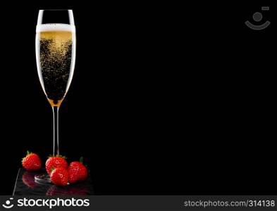 Elegant glass of yellow champagne with fresh stawberries on black marble board on black.