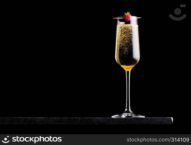 Elegant glass of yellow champagne with raspberry on stick on black marble board on black background.